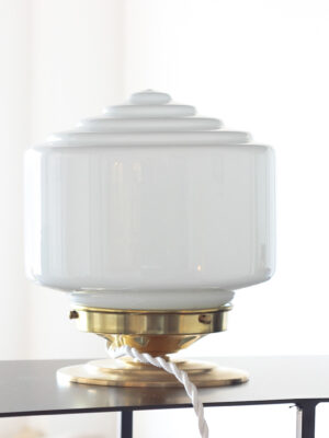 Table lamp composed of a cylindrical glass globe with an upper opaline glass tier on a brushed brass base. A modern black piece of furniture.