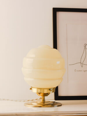 Lampe design sur meuble élégant. Globe en verre opaline sur base en laiton. Un cadre photo est derrière la lampe.