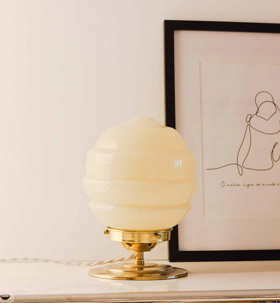 Candeeiro de design em móvel elegante. Globo de vidro opalino em base de latão. Uma moldura de foto está atrás do candeeiro.