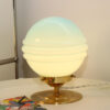 Lampe à poser composée d'un globe en verre vintage sphérique de couleur bleu turquoise - allumée sur un bureau.