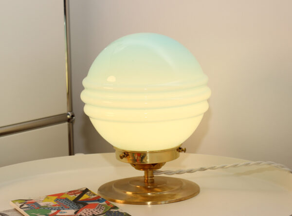 Lampe à poser composée d'un globe en verre vintage sphérique de couleur bleu turquoise - allumée sur un bureau.