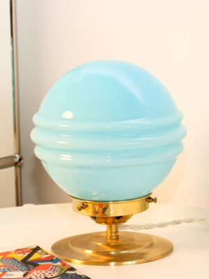Vintage blue glass lamp on nightstand. Table lamp composed of a spherical turquoise blue vintage glass globe - lit on a desk.