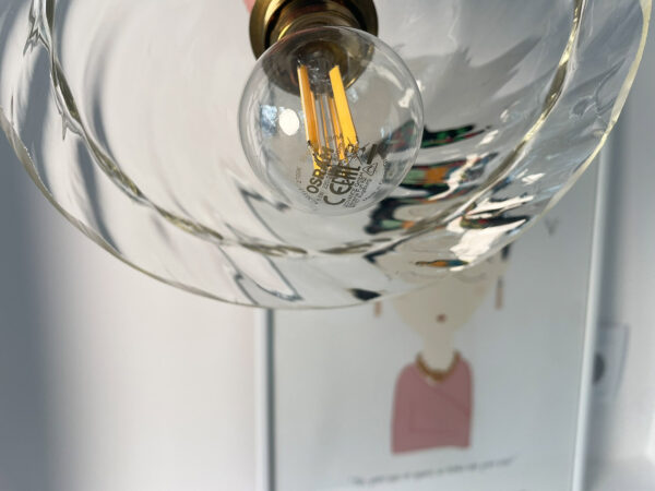 LED light bulb in decorative glass fixture. Hanging light above illustrated wall art. Artistic hanging lamp with a glass globe mounted on a brass socket above a wall drawing.