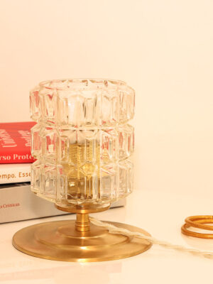 A bedside table lamp. The lamp consists of a vintage moulded glass globe resting on a brushed brass base.