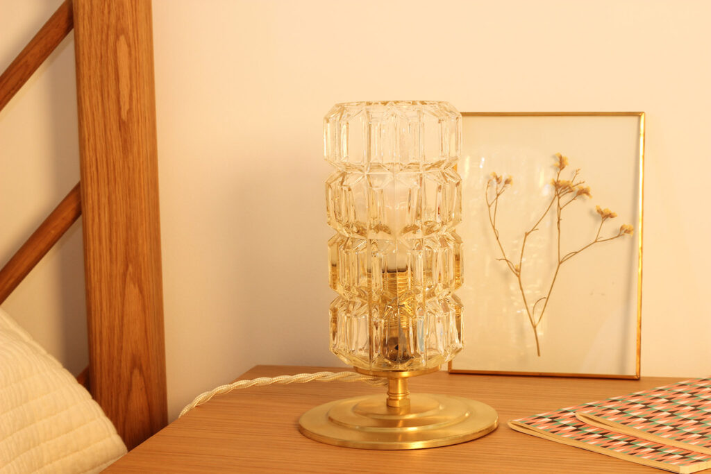 Lampe à poser sur une table de chevet en bois. La lampe à poser est composée d'un globe en verre vintage moulé et ciselé. Il repose sur une base en laiton brossé.