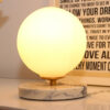 Lampe à poser en opaline, sphérique, lumineuse sur socle en marbre blanc et veines grises.
