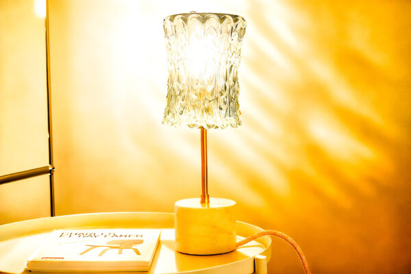 Vintage table lamp composed of a chiseled glass globe and a white marble base with beige veins. The lamp is illuminated.
