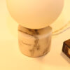 Lampe à poser en opaline, sphérique, lumineuse sur socle en marbre blanc et veines grises.