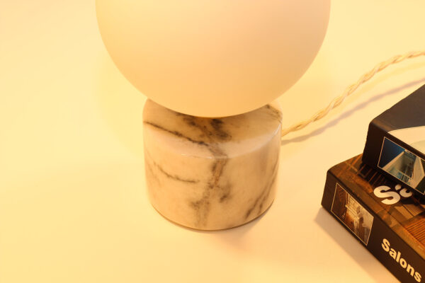 Lampe à poser en opaline, sphérique, lumineuse sur socle en marbre blanc et veines grises.