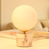 Lampe à poser en opaline, sphérique, lumineuse sur socle en marbre blanc et veines grises.