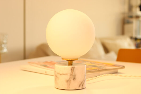 Lampe à poser en opaline, sphérique, lumineuse sur socle en marbre blanc et veines grises.