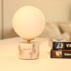Lampe à poser en opaline, sphérique, lumineuse sur socle en marbre blanc et veines grises.