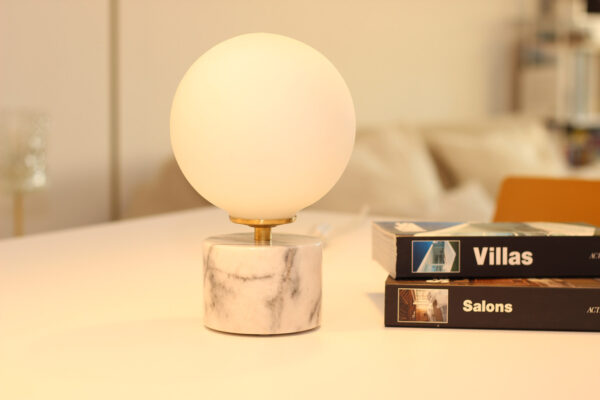 Lampe à poser en opaline, sphérique, lumineuse sur socle en marbre blanc et veines grises.
