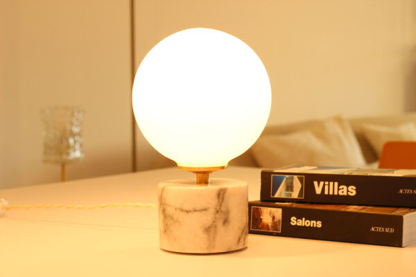 Lampe à poser en opaline, sphérique, lumineuse sur socle en marbre blanc et veines grises.