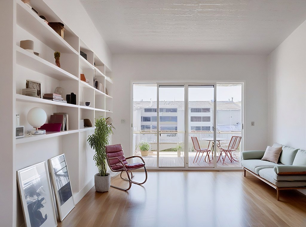 Salon minimaliste avec parquet bois clair, fauteuil vintage, canapé vert pastel et grande baie vitrée donnant sur un balcon.