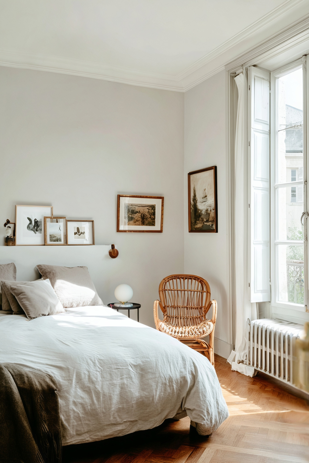 Chambre douce et lumineuse avec lit en lin, fauteuil en rotin et lampe Isabelle sur une table de chevet près de la fenêtre.