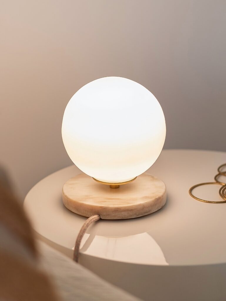 Lampe de chevet sphérique Isabelle en verre blanc diffusant une lumière douce sur une table de nuit