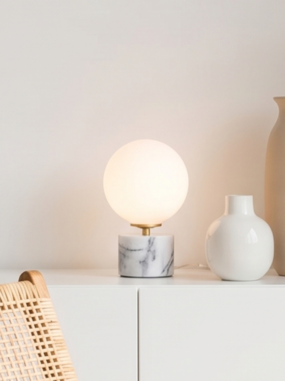 Laura ball lamp lit on a white sideboard in a minimalist living room — opaline globe and grey-veined Estremoz marble base — Alfama Chic