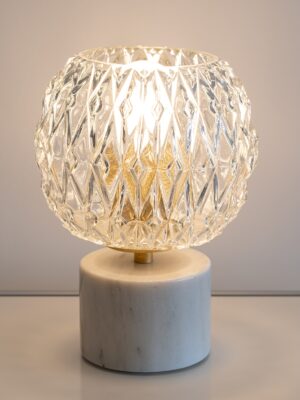 Candeeiro de mesa Emma com globo redondo em vidro facetado sobre base cilíndrica em mármore branco com subtis veios em tons bege