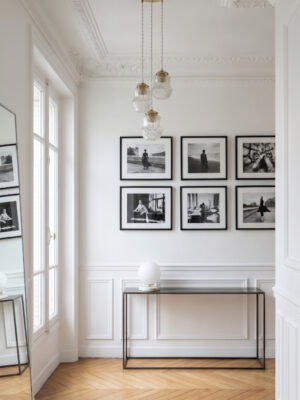 Triple vintage pendant light Louise at staggered heights in a Haussmann entrance hall, ceiling mouldings, black and white photo gallery, black console, herringbone parquet — Alfama Chic