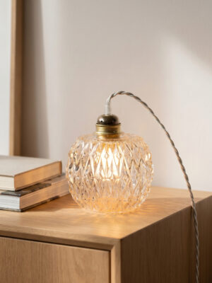 Vintage hand lamp Marie switched on placed on a light wood dresser, illuminated golden diamond pattern textured glass globe, twisted cord, stacked books — Alfama Chic